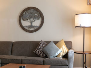 gray sofa sectional with accent pillows, coffee table with coasters, side table with lamp, and wall wooden cut out of tree wall decor.