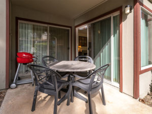 Four black patio chairs with black and gray patio table, red barbecue grill on ground level outdoor patio