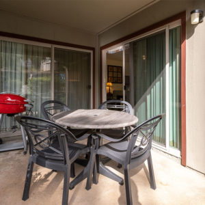 Four black patio chairs with black and gray patio table, red barbecue grill on ground level outdoor patio