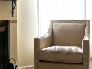 studded beige upholstered accent chair by natural light window