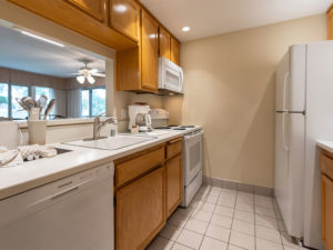 vacation condo full kitchen with white refrigerator, microwave, electric oven range, coffee maker, and dishwasher. Kitchen sing with metal cooking utensils