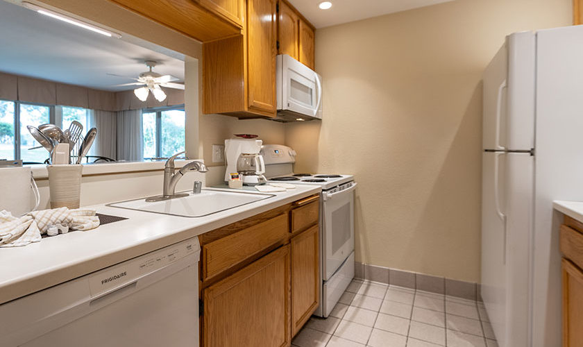 vacation condo full kitchen with white refrigerator, microwave, electric oven range, coffee maker, and dishwasher. Kitchen sing with metal cooking utensils