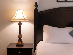 San Diego Country Estates master bedroom detail. With dark brown headboard and nightstand with table lamp and white pillows and white bed linen