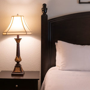 San Diego Country Estates master bedroom detail. With dark brown headboard and nightstand with table lamp and white pillows and white bed linen